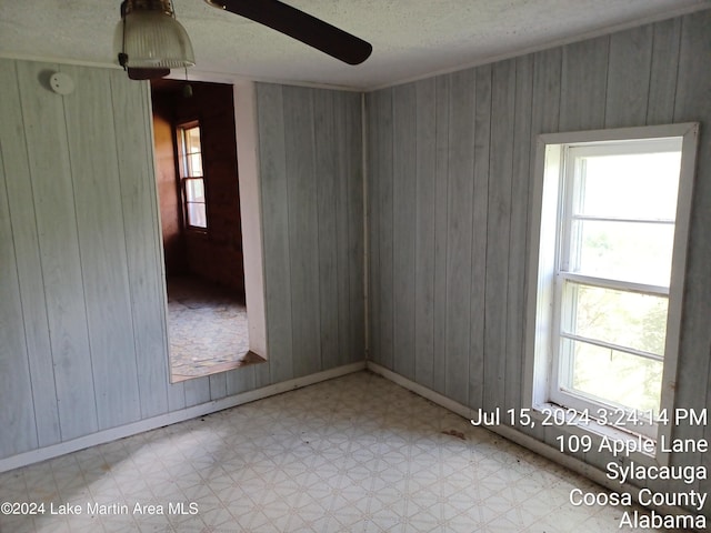 spare room with ceiling fan, a textured ceiling, and wooden walls