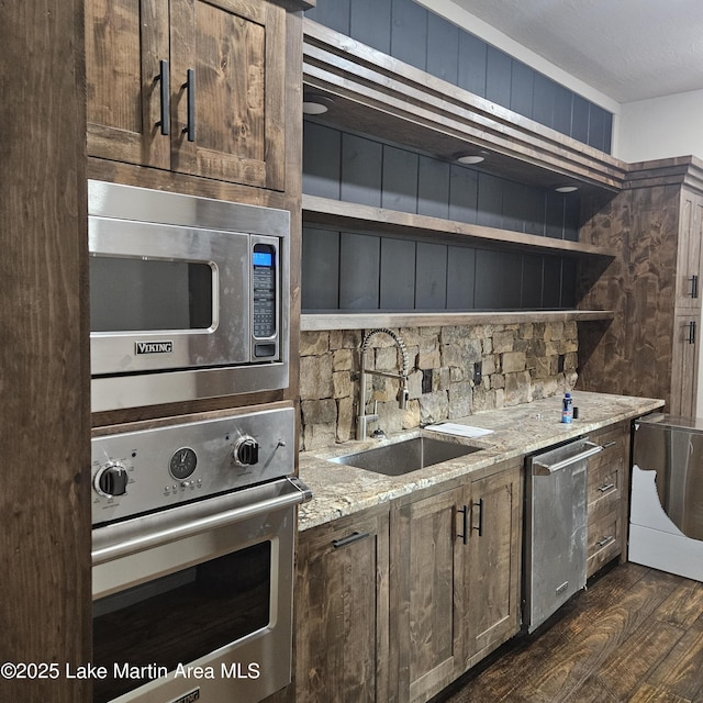 kitchen with light stone counters, open shelves, appliances with stainless steel finishes, dark wood-type flooring, and a sink