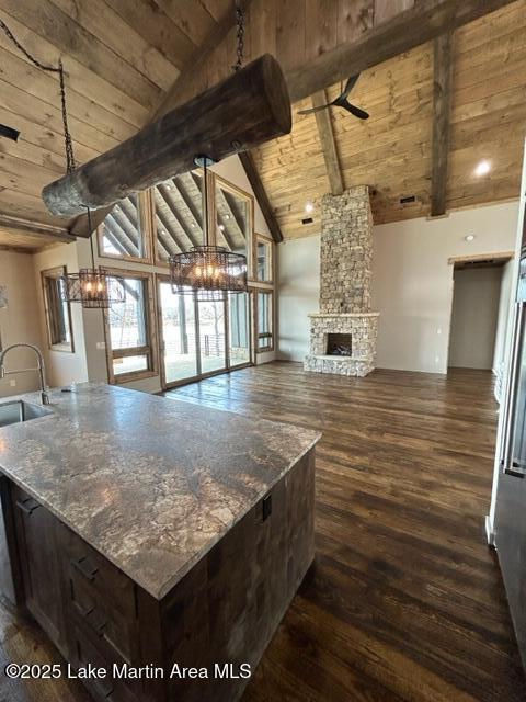 kitchen featuring wooden ceiling, open floor plan, dark wood-style flooring, a stone fireplace, and beam ceiling