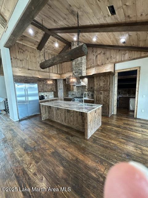 kitchen with dark wood-style flooring, beam ceiling, wood ceiling, a sink, and a large island with sink