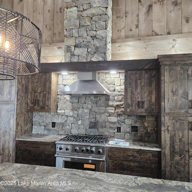 kitchen featuring stone countertops, high end stainless steel range oven, wall chimney range hood, and dark brown cabinets