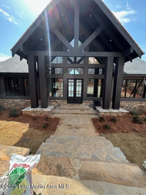 entrance to property featuring a shingled roof, french doors, and stone siding