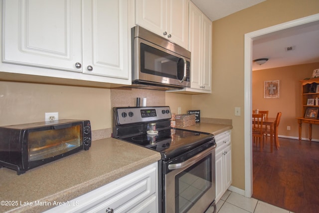 kitchen with stainless steel appliances, white cabinets, light countertops, light tile patterned floors, and baseboards