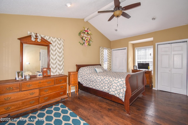 bedroom featuring baseboards, lofted ceiling with beams, dark wood-style flooring, ceiling fan, and two closets