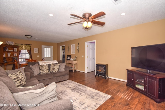 living area featuring a textured ceiling, a wood stove, baseboards, and dark wood-style flooring