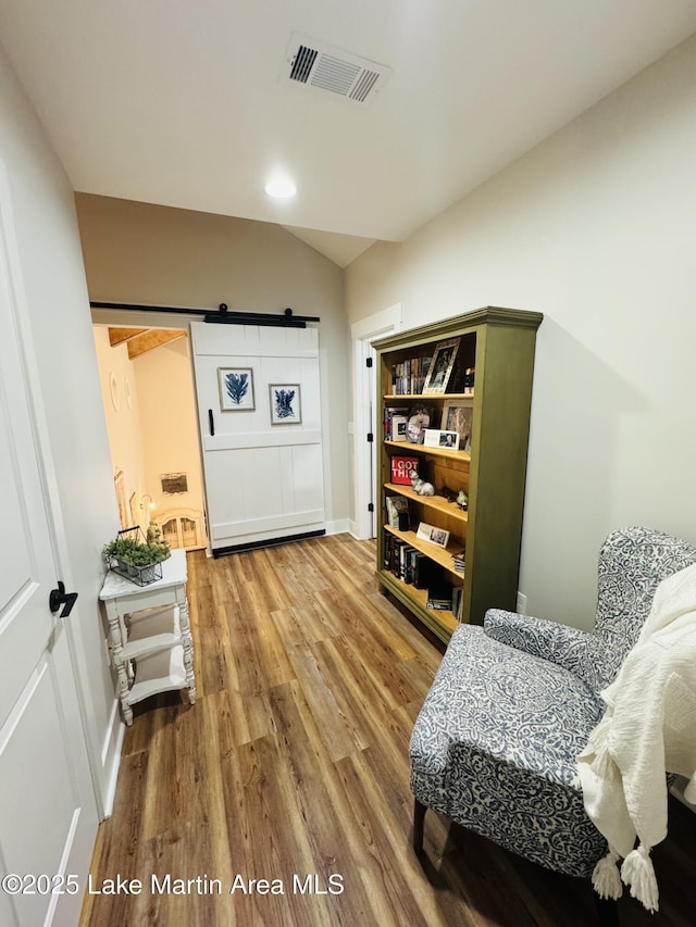 living area featuring wood-type flooring, a barn door, and lofted ceiling