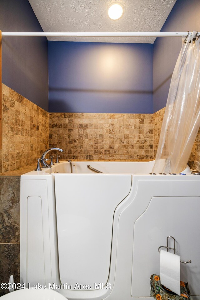 bathroom featuring a tub to relax in, a textured ceiling, and tile walls