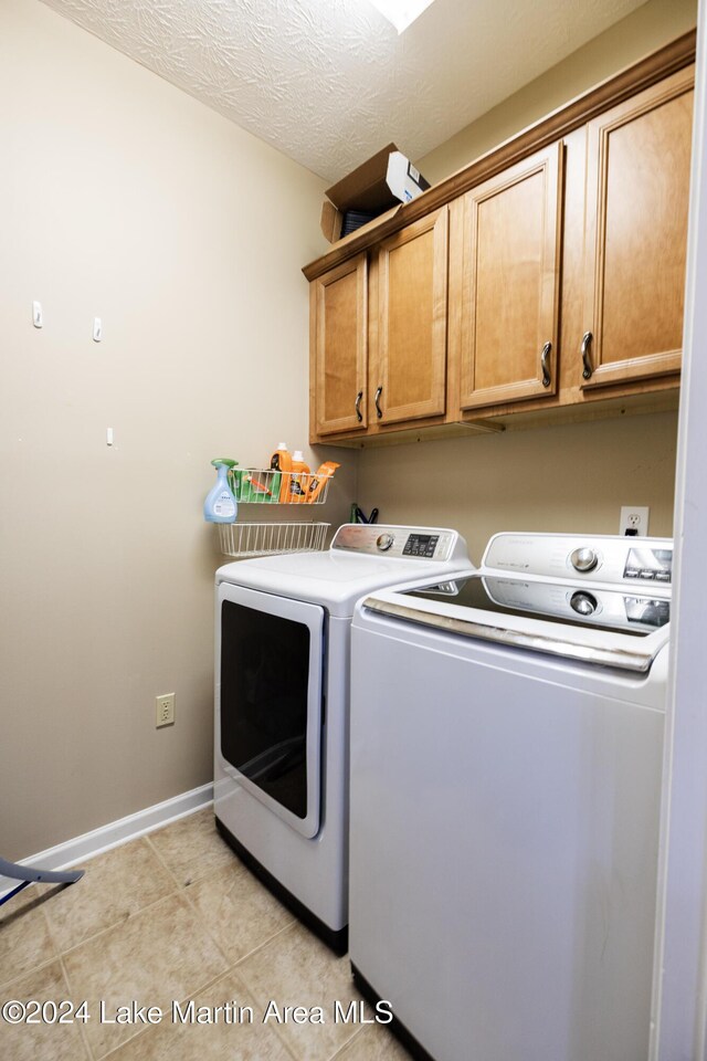 washroom with washing machine and clothes dryer, light tile patterned floors, cabinets, and a textured ceiling