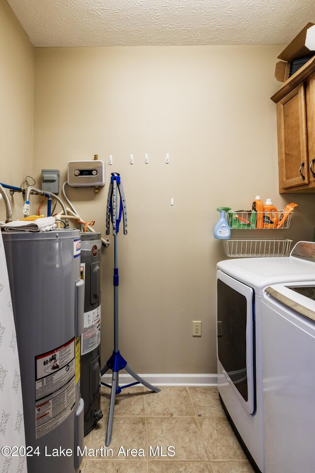 washroom with cabinets, a textured ceiling, water heater, light tile patterned flooring, and washing machine and clothes dryer