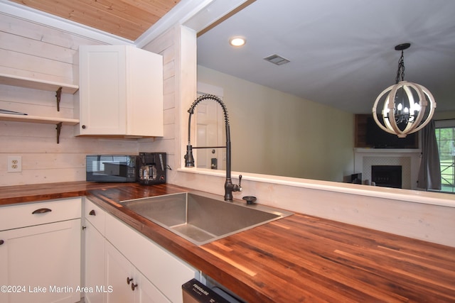 kitchen featuring decorative light fixtures, sink, white cabinetry, and wood counters