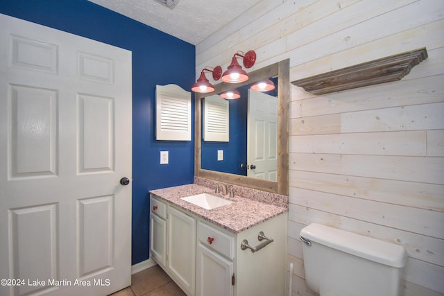 bathroom with toilet, wooden walls, tile patterned flooring, a textured ceiling, and vanity