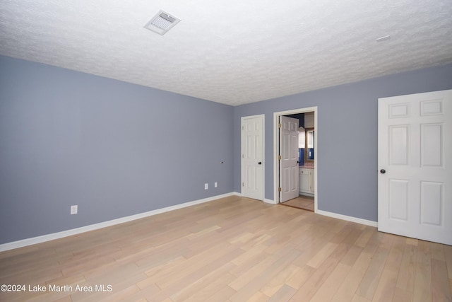 unfurnished bedroom with ensuite bath, light wood-type flooring, and a textured ceiling