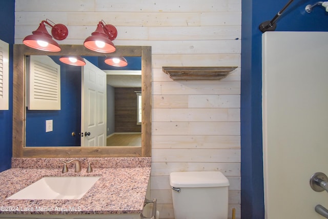 bathroom featuring toilet, wood walls, and vanity