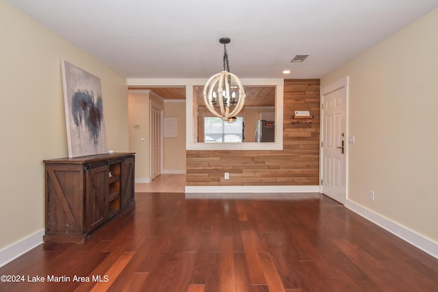 unfurnished dining area featuring a notable chandelier, wood walls, and dark hardwood / wood-style floors