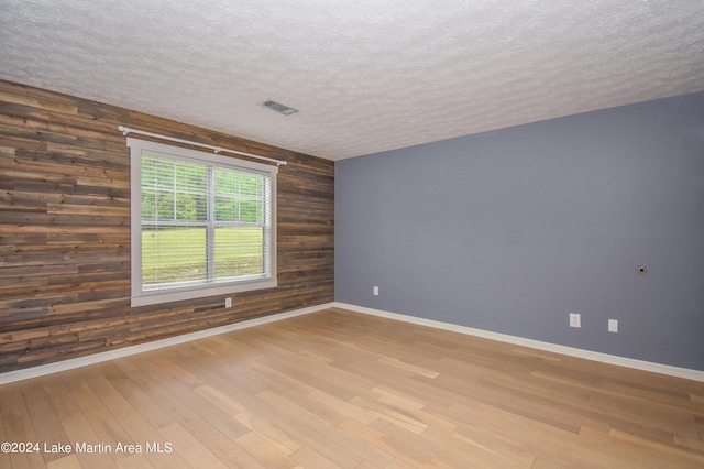 empty room featuring wooden walls, a textured ceiling, and hardwood / wood-style flooring