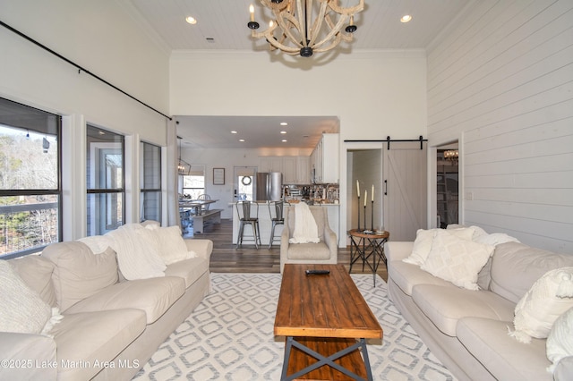 living room with a high ceiling, ornamental molding, a chandelier, and a barn door