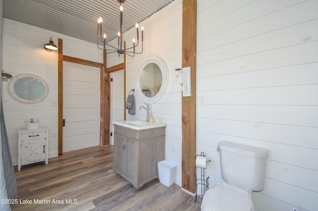 bathroom with hardwood / wood-style flooring, wood walls, a notable chandelier, toilet, and vanity