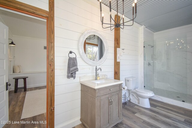 bathroom with wood-type flooring, a notable chandelier, vanity, a tile shower, and toilet