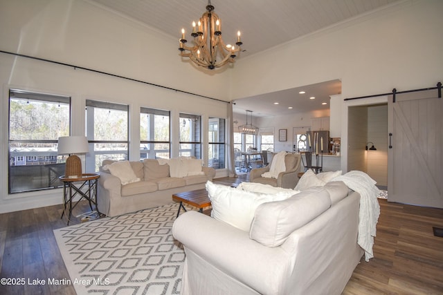 living room with hardwood / wood-style floors, an inviting chandelier, a towering ceiling, a barn door, and ornamental molding