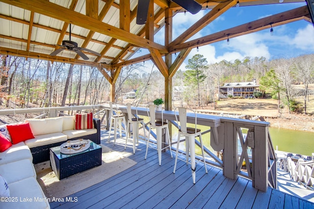 wooden deck featuring a water view, an outdoor bar, ceiling fan, and an outdoor living space