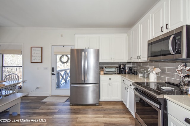 kitchen featuring stainless steel appliances, backsplash, ornamental molding, white cabinetry, and dark hardwood / wood-style floors