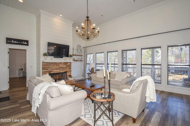 living room featuring hardwood / wood-style flooring, a notable chandelier, a stone fireplace, a high ceiling, and crown molding