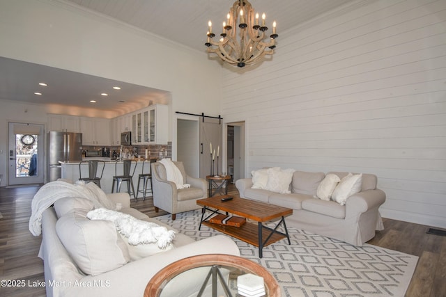 living room with an inviting chandelier, light hardwood / wood-style flooring, crown molding, a barn door, and a high ceiling