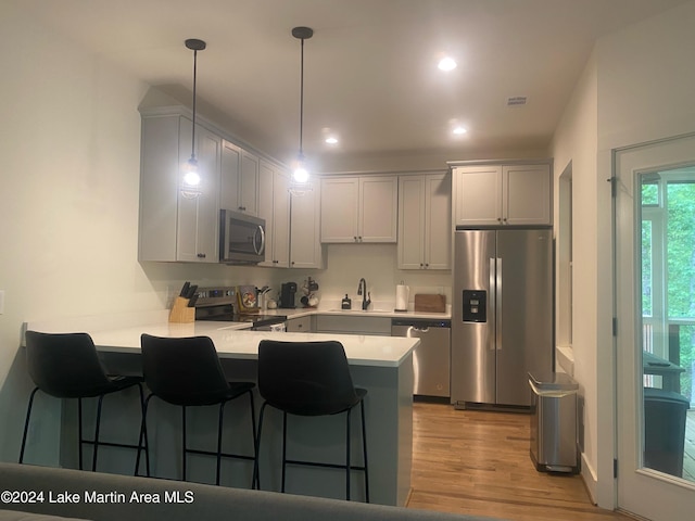 kitchen featuring sink, hanging light fixtures, kitchen peninsula, appliances with stainless steel finishes, and light wood-type flooring