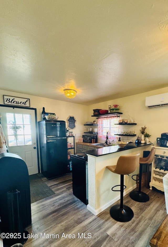 kitchen with dark hardwood / wood-style flooring, an AC wall unit, a breakfast bar, and refrigerator