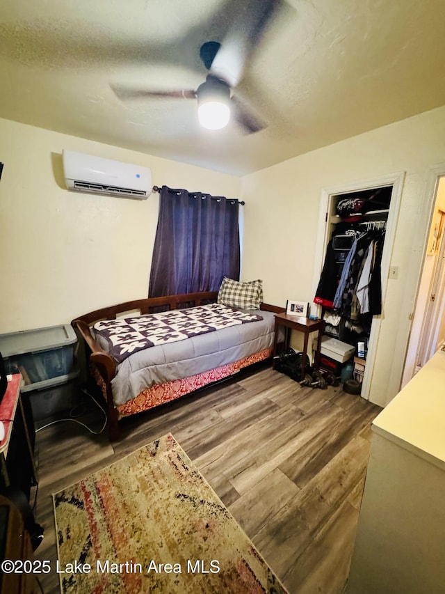 bedroom with hardwood / wood-style flooring, a textured ceiling, an AC wall unit, and ceiling fan