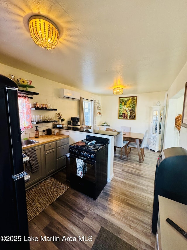 kitchen with hardwood / wood-style floors, sink, a wall unit AC, black appliances, and a textured ceiling