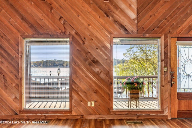 doorway to outside featuring hardwood / wood-style flooring, vaulted ceiling, a water view, and wood walls