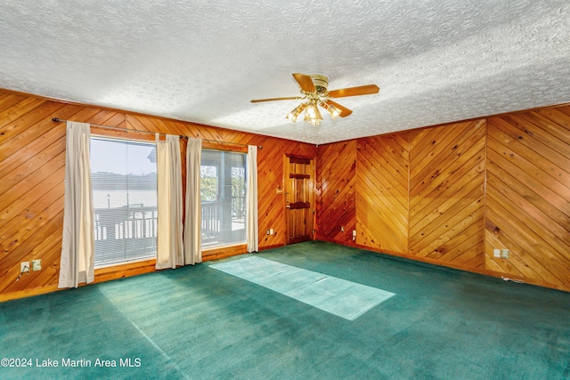 spare room featuring dark colored carpet, a water view, ceiling fan, and wooden walls