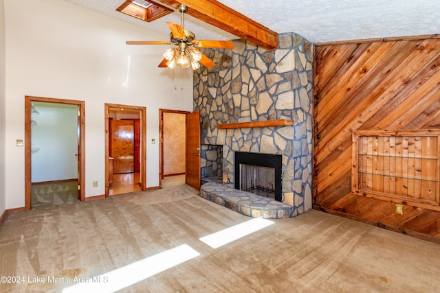 unfurnished living room featuring carpet, wood walls, a stone fireplace, and a high ceiling