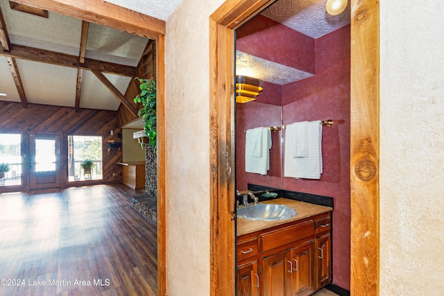 bathroom featuring hardwood / wood-style floors, vanity, wood walls, and vaulted ceiling with beams