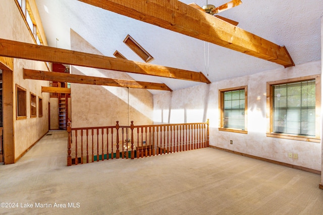 carpeted empty room with beam ceiling, a textured ceiling, high vaulted ceiling, and ceiling fan