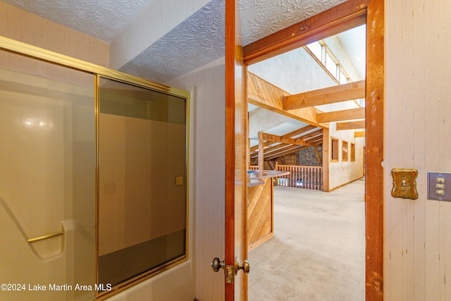 bathroom featuring wood walls, enclosed tub / shower combo, and a textured ceiling