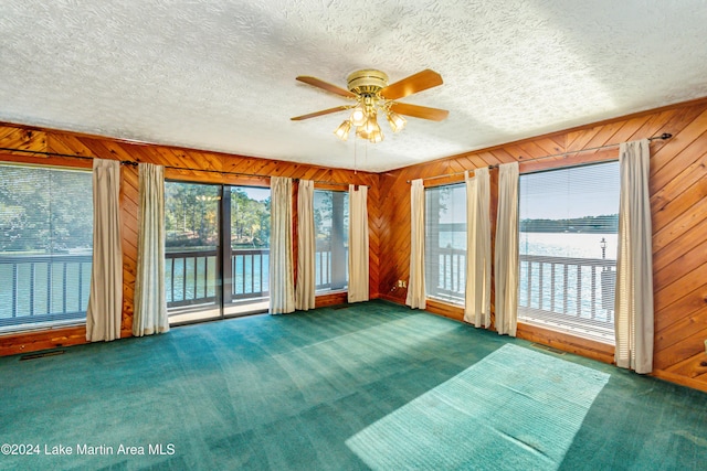 interior space with wood walls, dark carpet, a water view, ceiling fan, and a textured ceiling