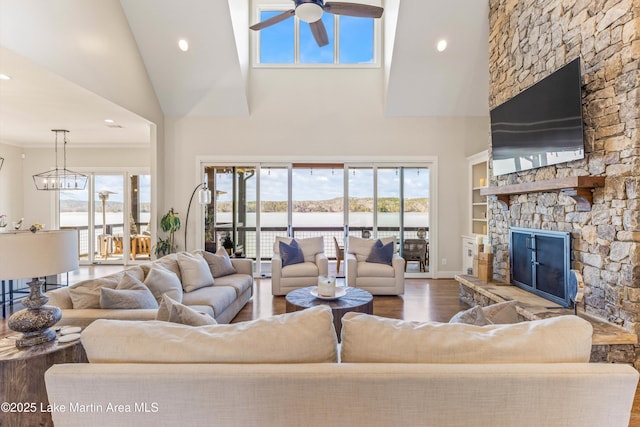 living room featuring ceiling fan with notable chandelier, a stone fireplace, plenty of natural light, and wood finished floors