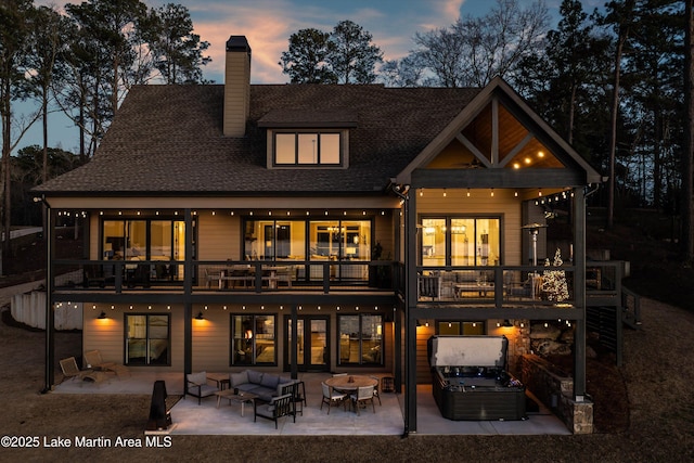 2082 River Oaks Dr, Jacksons Gap, AL 36861 - back of property at dusk featuring an outdoor living space, a patio area, a hot tub, a balcony, and a chimney