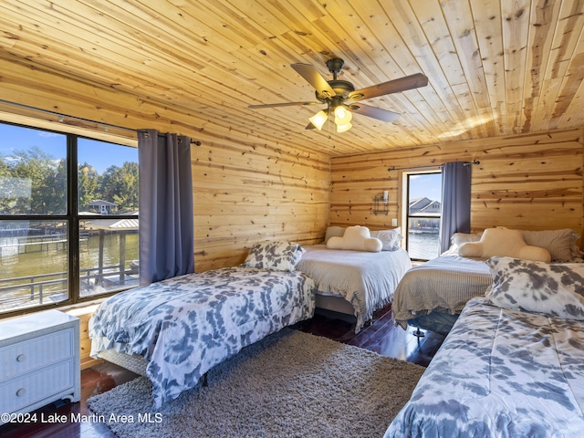 bedroom featuring wood walls, hardwood / wood-style flooring, ceiling fan, a water view, and wooden ceiling