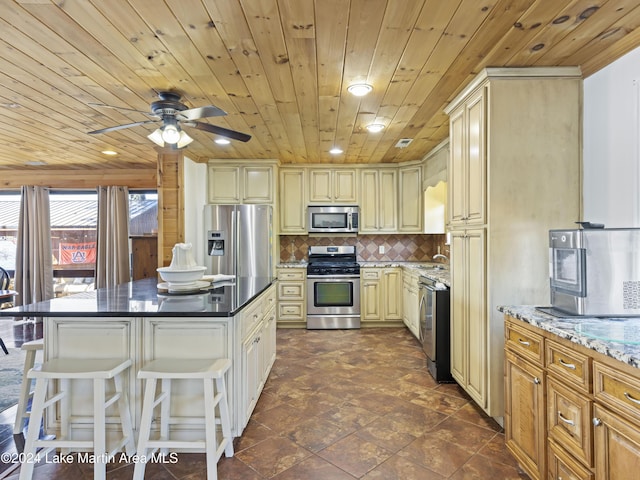 kitchen with a kitchen bar, wooden ceiling, appliances with stainless steel finishes, cream cabinets, and backsplash