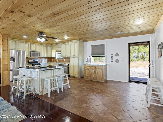 kitchen with backsplash, a kitchen bar, dark tile patterned floors, stainless steel appliances, and a healthy amount of sunlight