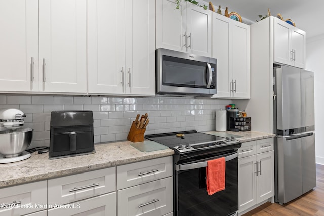 kitchen featuring white cabinets, decorative backsplash, light hardwood / wood-style floors, light stone counters, and stainless steel appliances