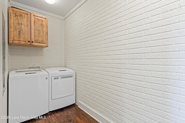 laundry area with washing machine and dryer, dark hardwood / wood-style flooring, brick wall, and cabinets