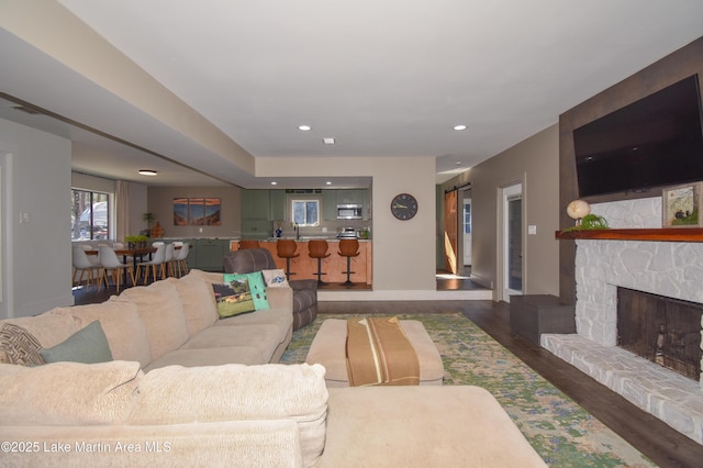 living area featuring a stone fireplace, recessed lighting, wood finished floors, and baseboards
