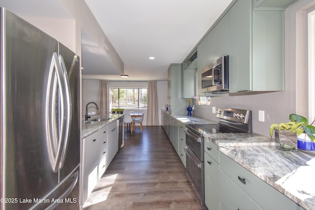 kitchen with a sink, recessed lighting, stainless steel appliances, light stone countertops, and dark wood-style flooring