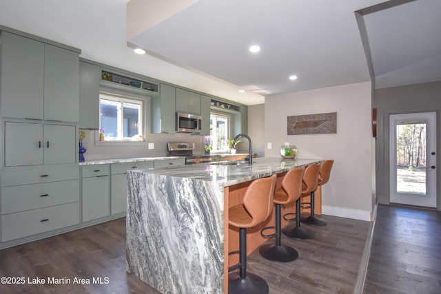 kitchen with light stone countertops, a breakfast bar, dark wood finished floors, a sink, and appliances with stainless steel finishes