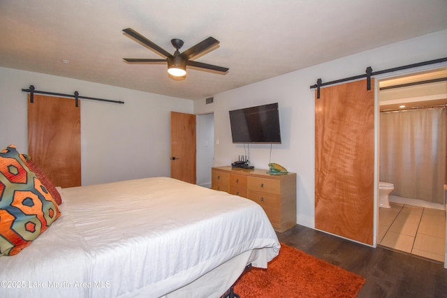 bedroom with wood finished floors, visible vents, ceiling fan, a barn door, and connected bathroom