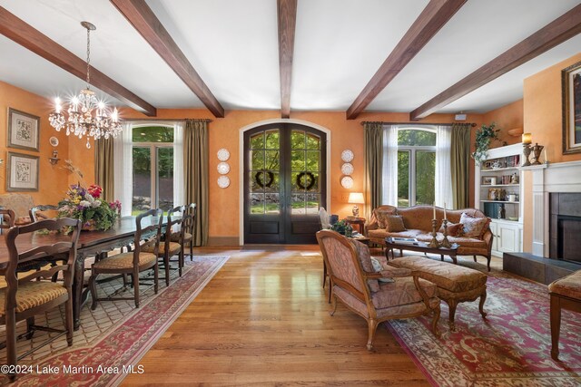 living room featuring beamed ceiling, an inviting chandelier, french doors, and light wood-type flooring